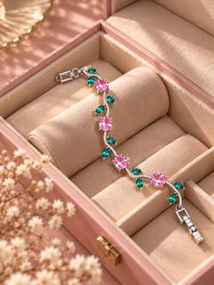 A silver-toned bracelet with pink and green gemstones displayed inside a blush pink jewelry box with beige cushioning.
