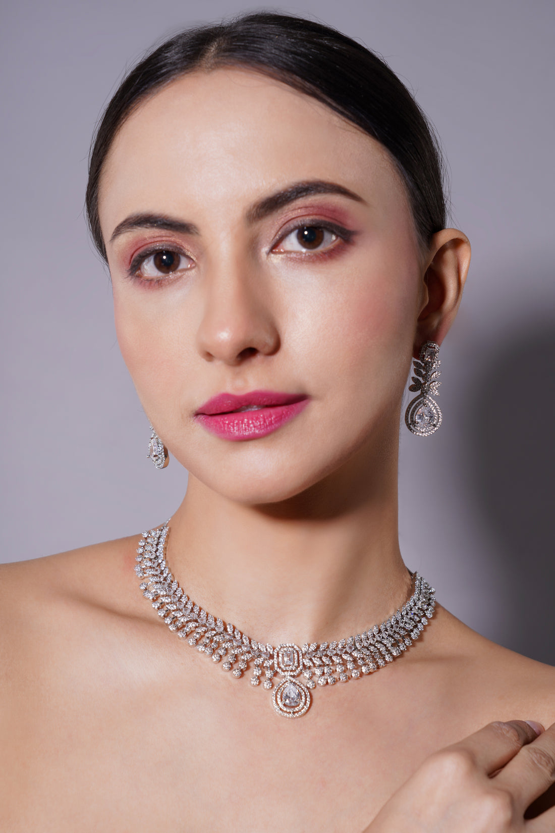 Woman wearing a silver necklace and earrings against a gray background