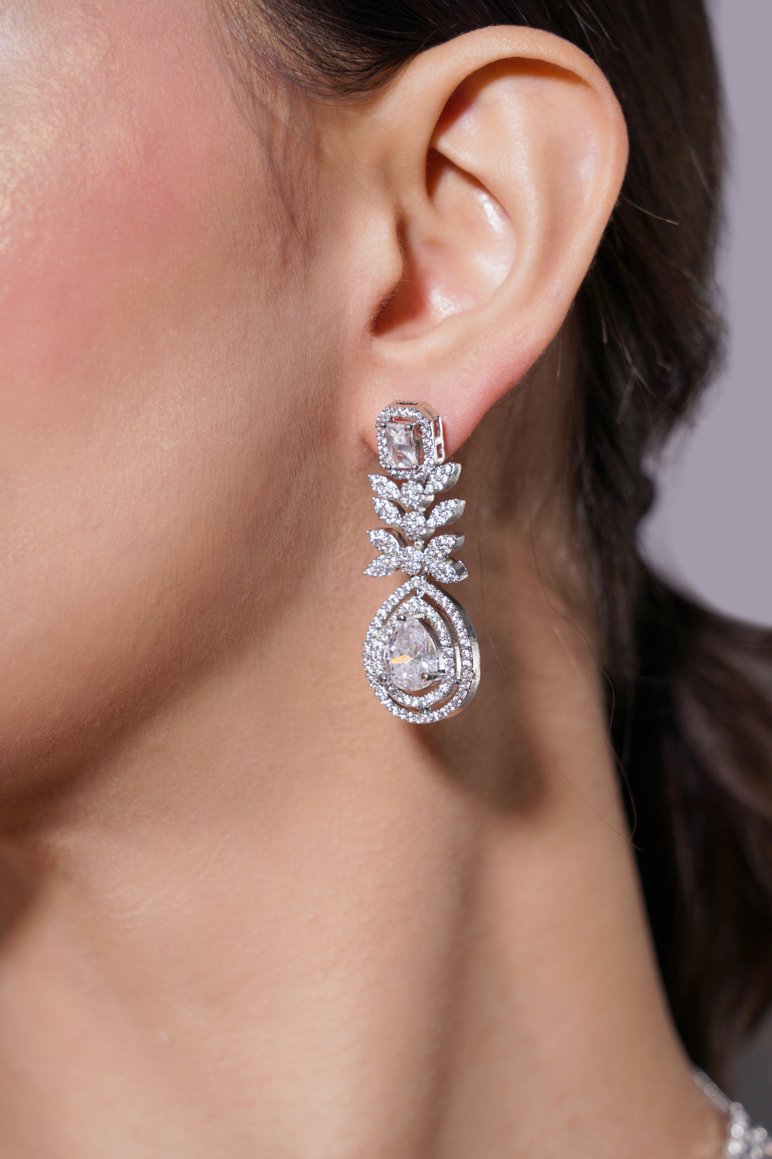 Close-up of a diamond earring on an ear with a neutral background