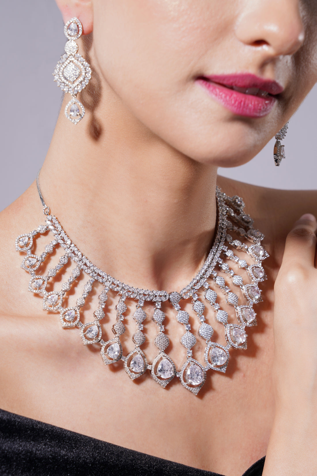 Close-up of a woman wearing a sparkling diamond necklace and earrings against a neutral background.