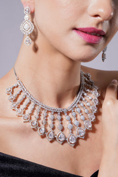 Close-up of a woman wearing a sparkling diamond necklace and earrings against a neutral background.