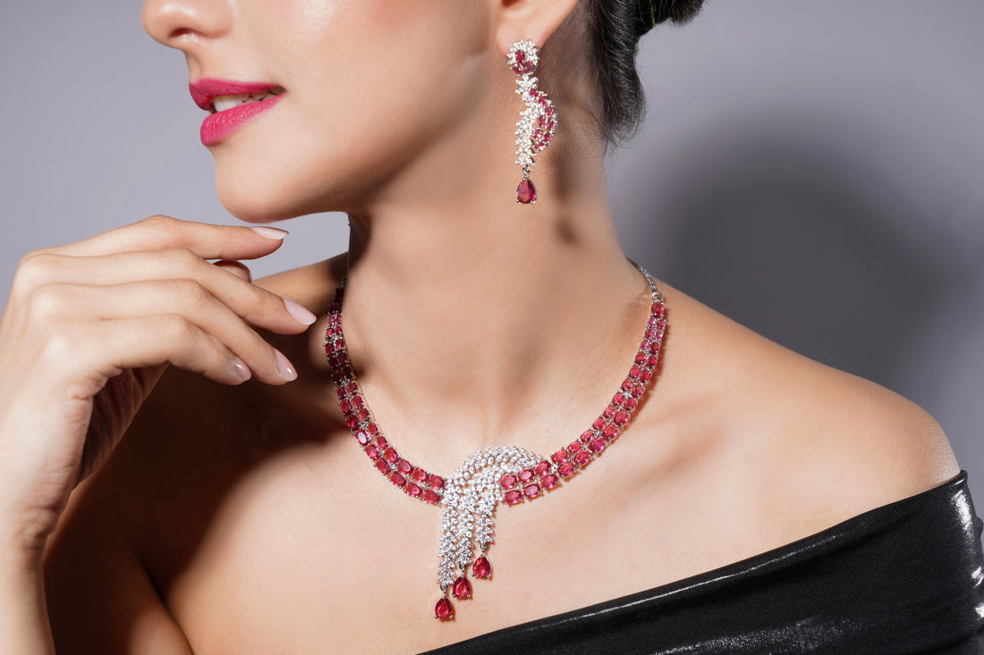 Close-up of a woman wearing a red gemstone necklace and earrings against a neutral background