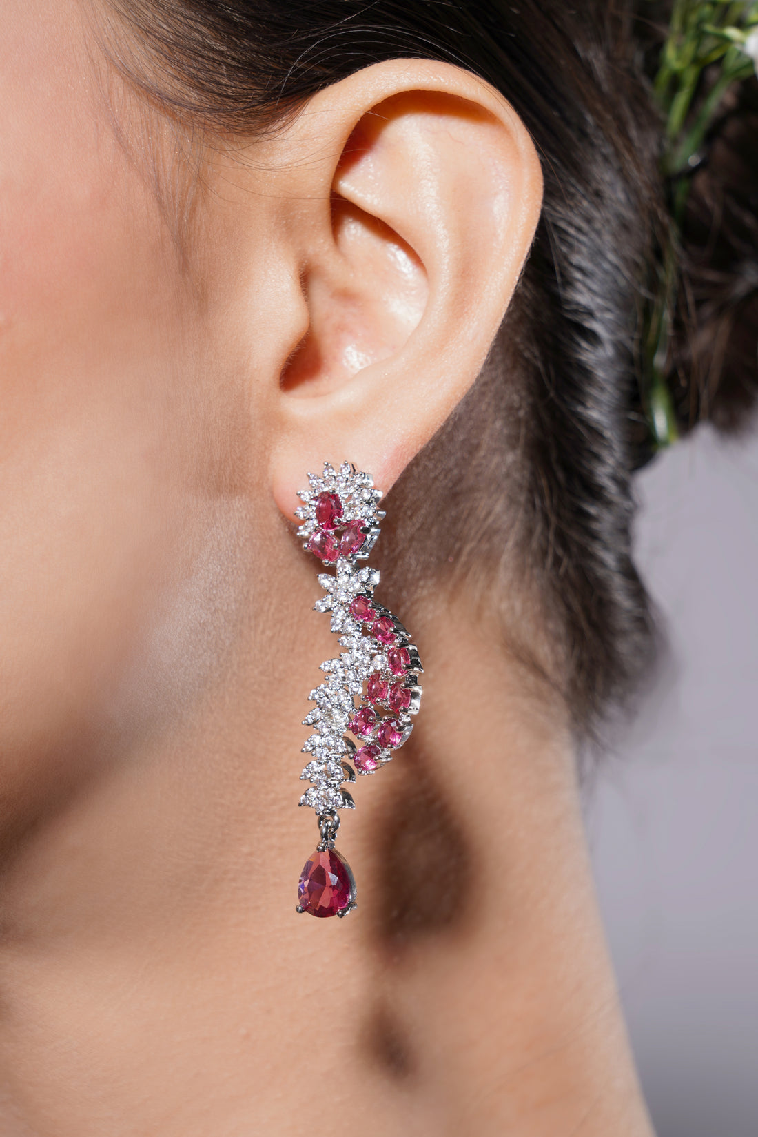 Close-up of a woman's ear wearing a sparkling earring with pink gemstones.