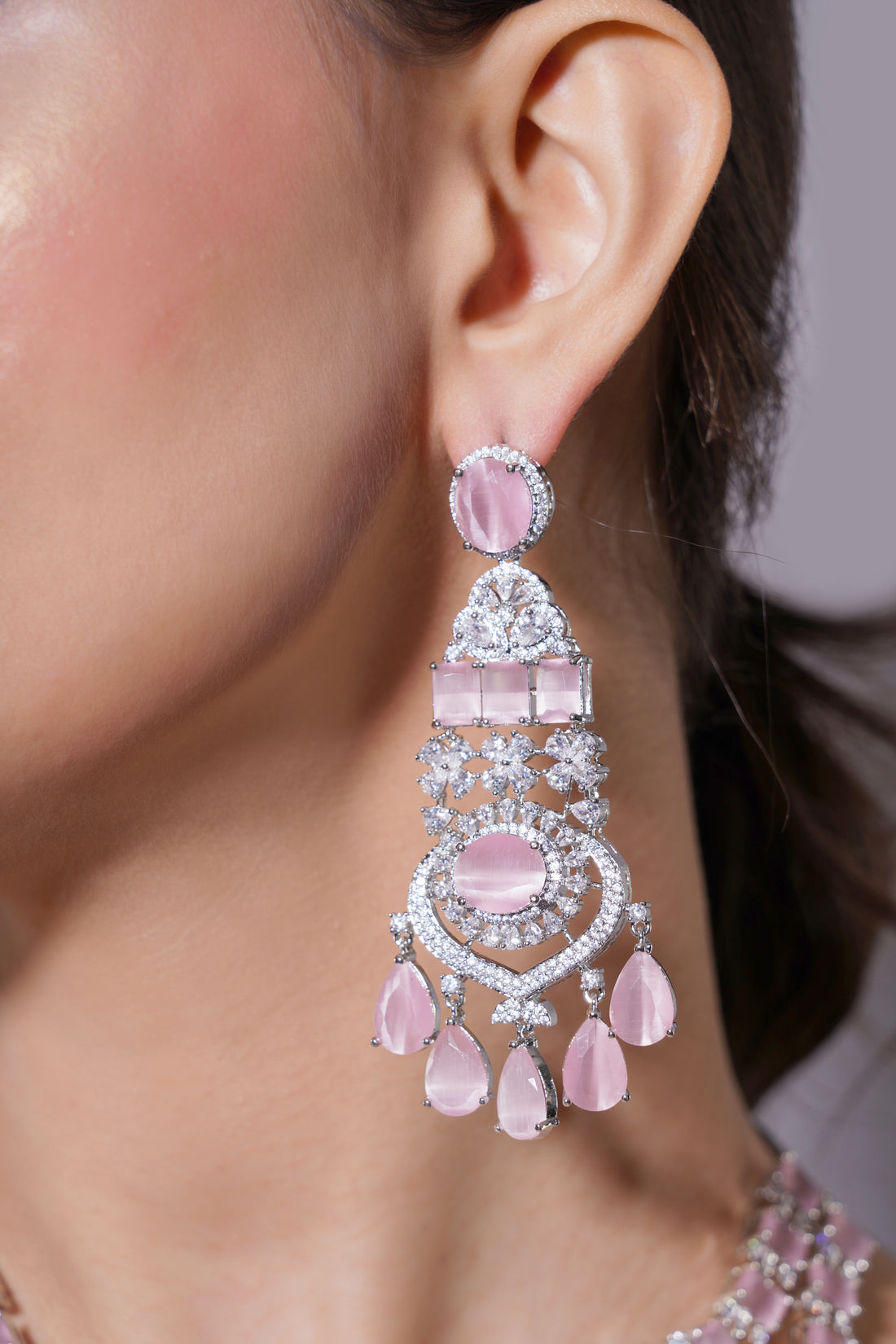 Close-up of a person wearing pink chandelier earrings with a blurred background