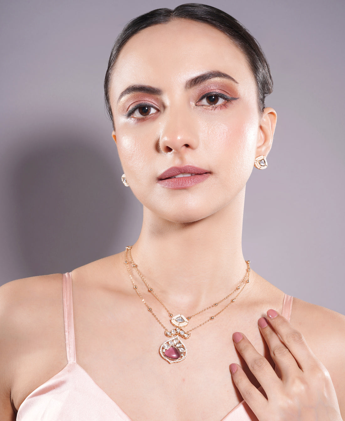 Woman wearing jewelry including a necklace, earrings, and ring on a plain background