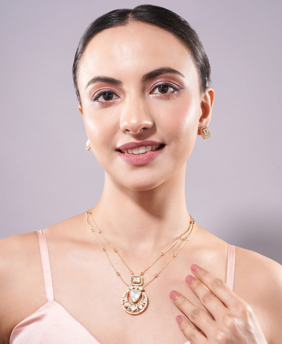 Woman wearing a gold necklace with a heart pendant against a plain background