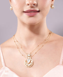 Close-up of a woman wearing a gold necklace with a heart-shaped pendant on a gray background