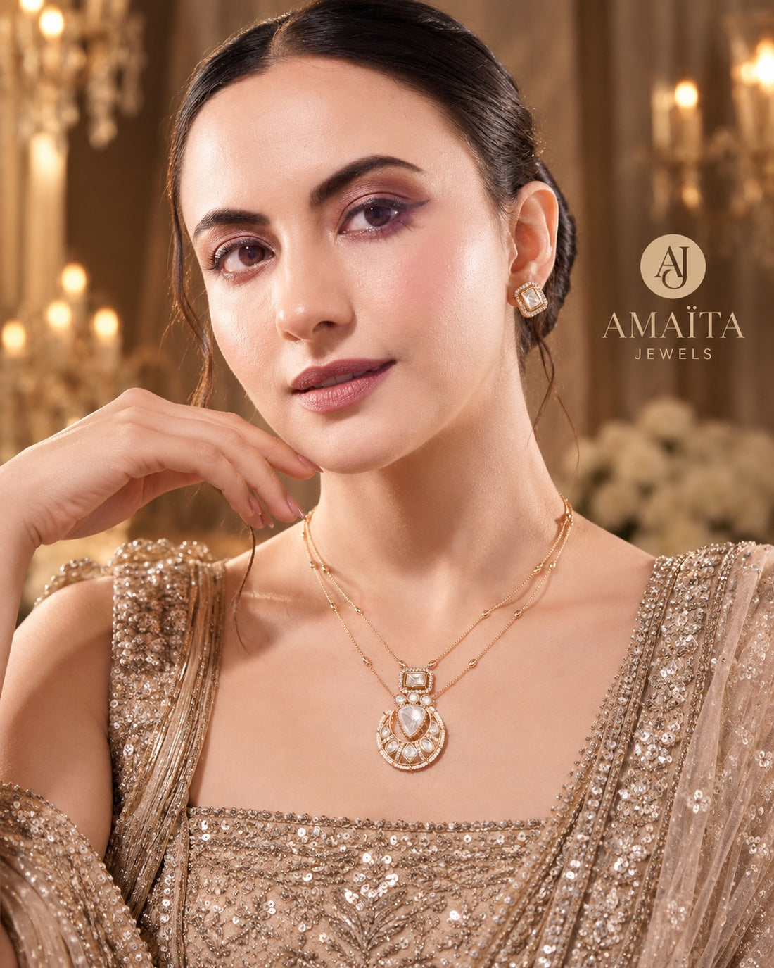 A woman wearing a gold-tone necklace and matching stud earring with a pearl-like center, styled with a sequined beige gown in an elegant indoor setting. The brand name 'AMAITA JEWELS' is visible in the upper right.
