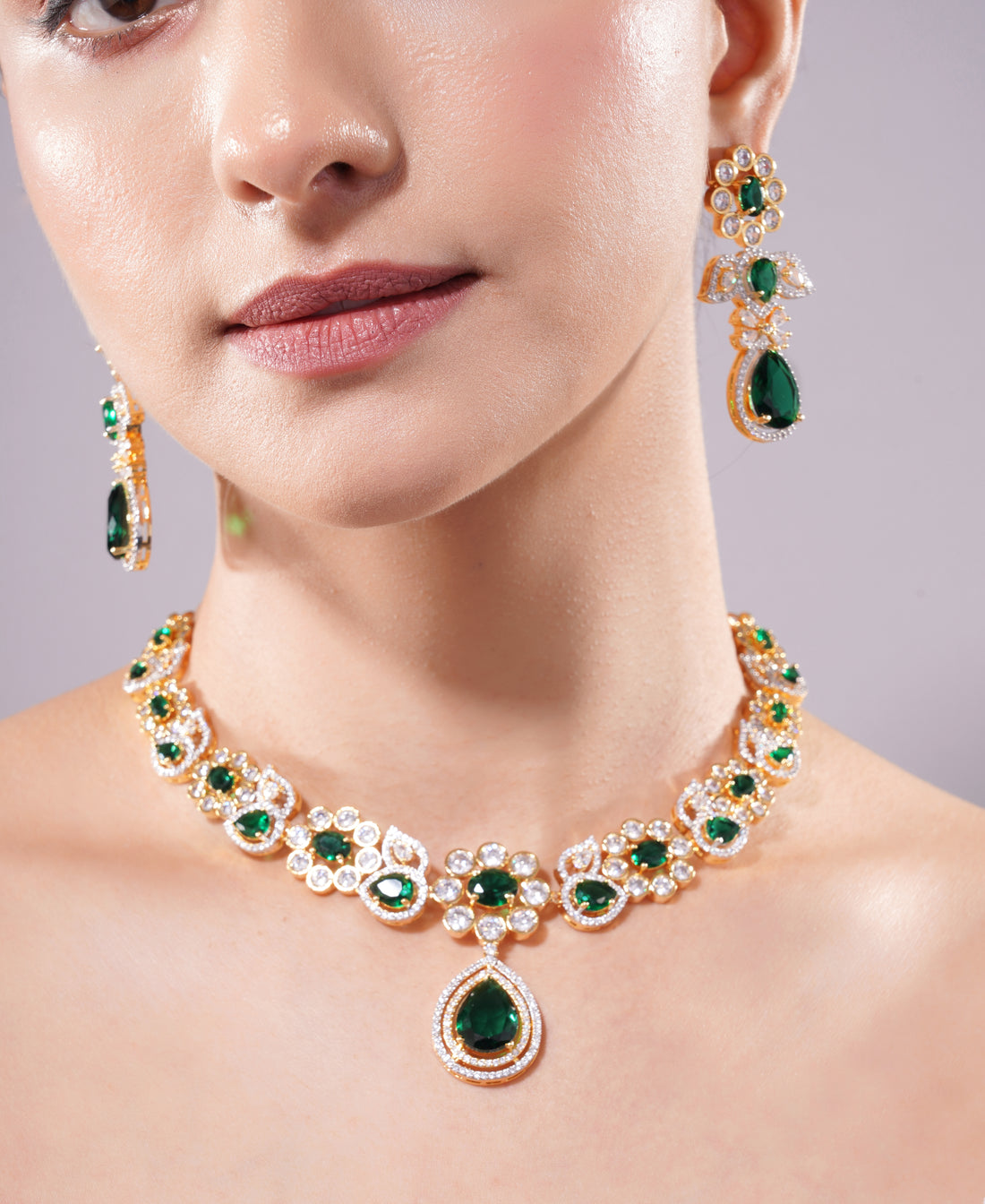 Close-up of a woman wearing a green gemstone necklace and earrings on a neutral background