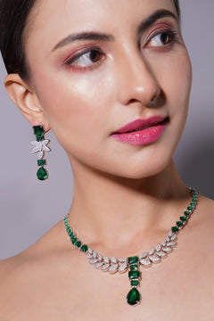 Woman wearing a green and silver necklace and earrings against a gray background