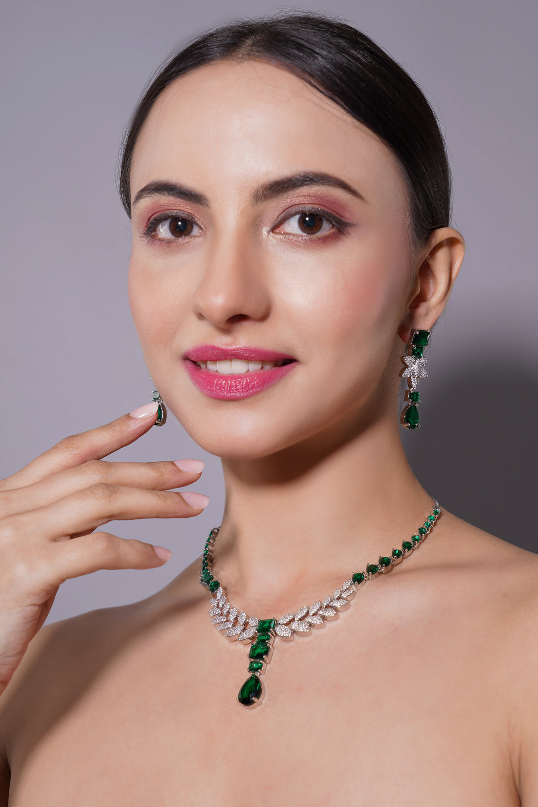 Woman wearing a green and silver necklace and earrings against a gray background