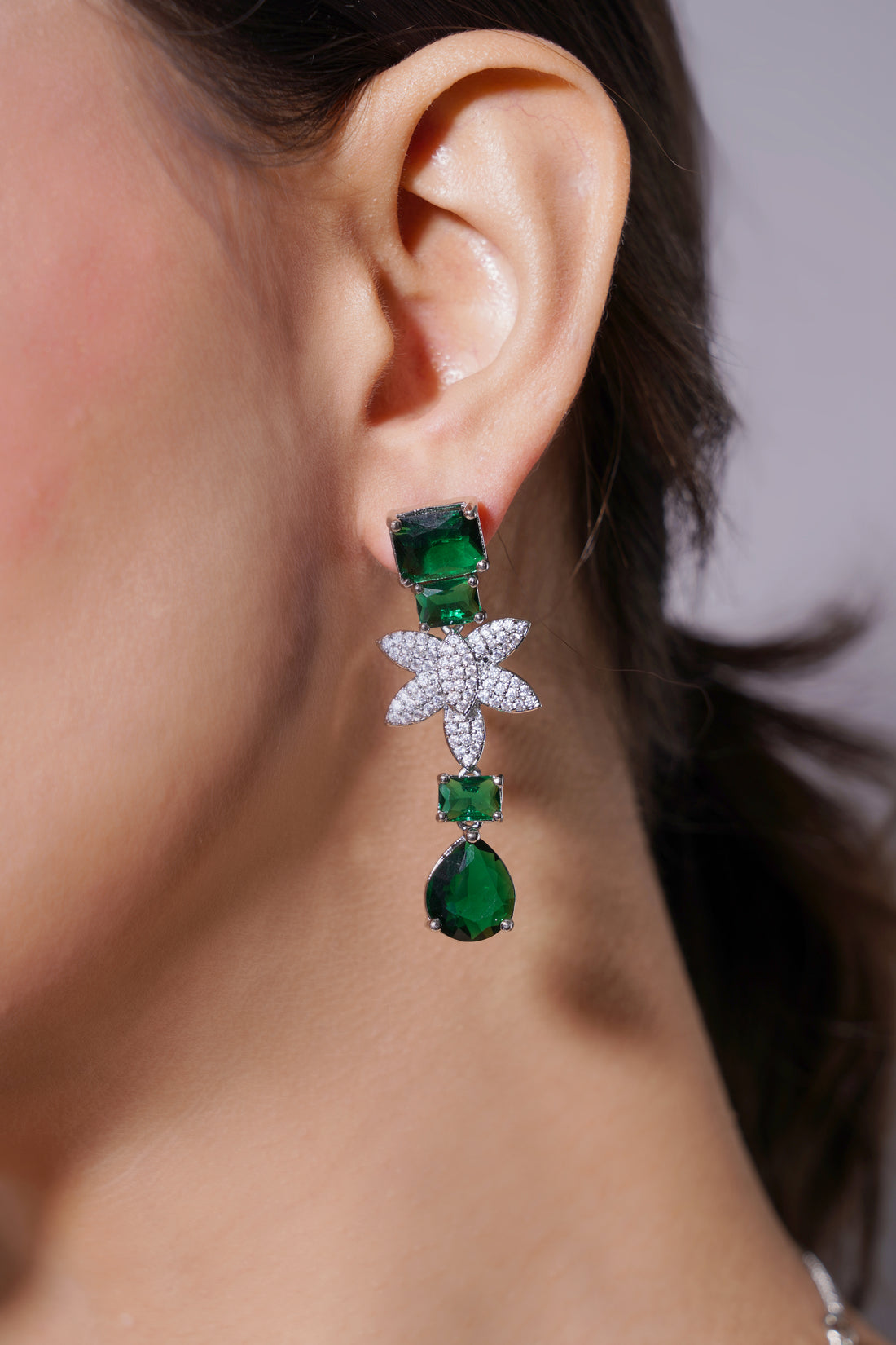 Close-up of a person wearing a star-shaped earring with green gemstones.