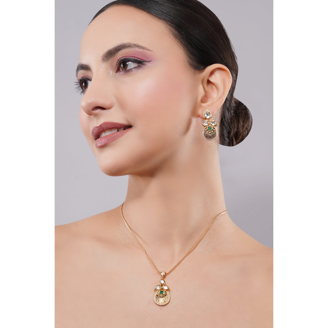 Woman wearing a gold necklace and earrings against a gray background