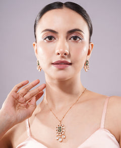 Woman wearing gold jewelry with green detailing including earrings and a necklace on a plain background