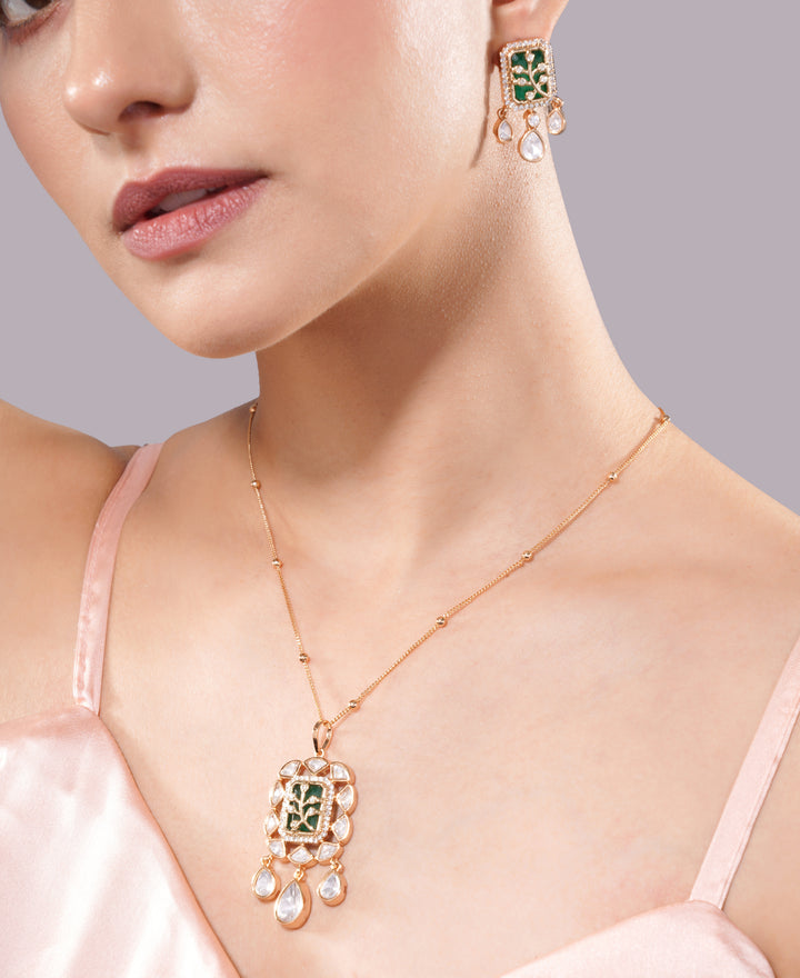 Close-up of a woman wearing a gold necklace and earrings with green gemstones on a gray background. jewellery set, pendant with chain, pendant set, pendants