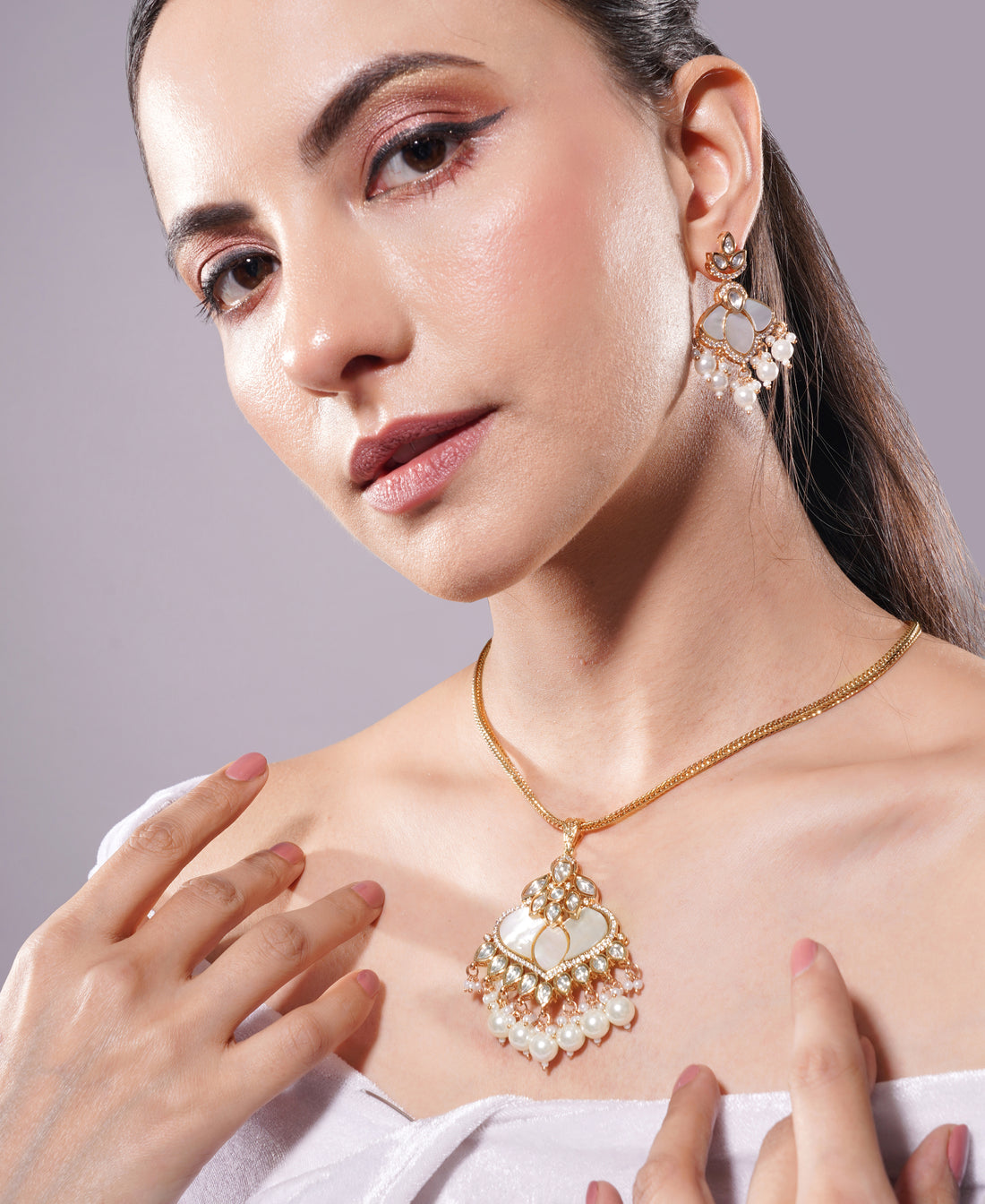 Woman wearing a gold necklace and earrings against a gray background