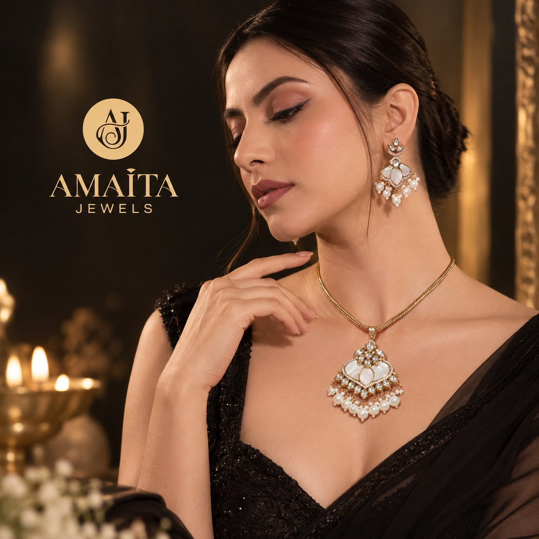 A woman wearing an ornate gold and pearl pendant necklace with matching drop earrings, posed in a black embellished dress against a warm, candle-lit background. The brand logo 'AMAITA JEWELS' is visible in the upper left.
