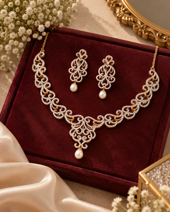Gold filigree necklace and matching drop earrings with white pearl accents, displayed on a dark red velvet jewelry box with decorative flowers and satin fabric around it.