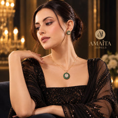 A woman wearing a gold necklace with a green and white stone pendant and matching green stone earrings, posed in a luxurious room with warm lighting. The brand logo 'AMAÍTA JEWELS' is visible on the right.