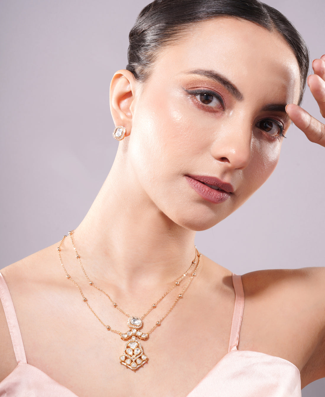 Woman wearing a gold necklace with a pendant against a neutral background