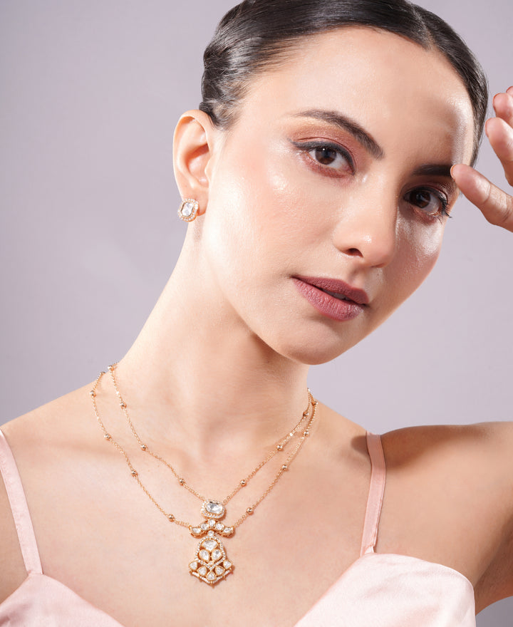 Woman wearing a gold necklace with a pendant against a neutral background