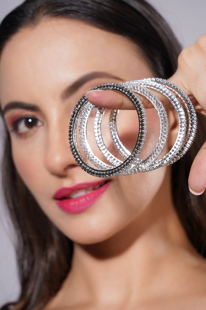 Woman holding silver bangles in front of her face against a neutral background