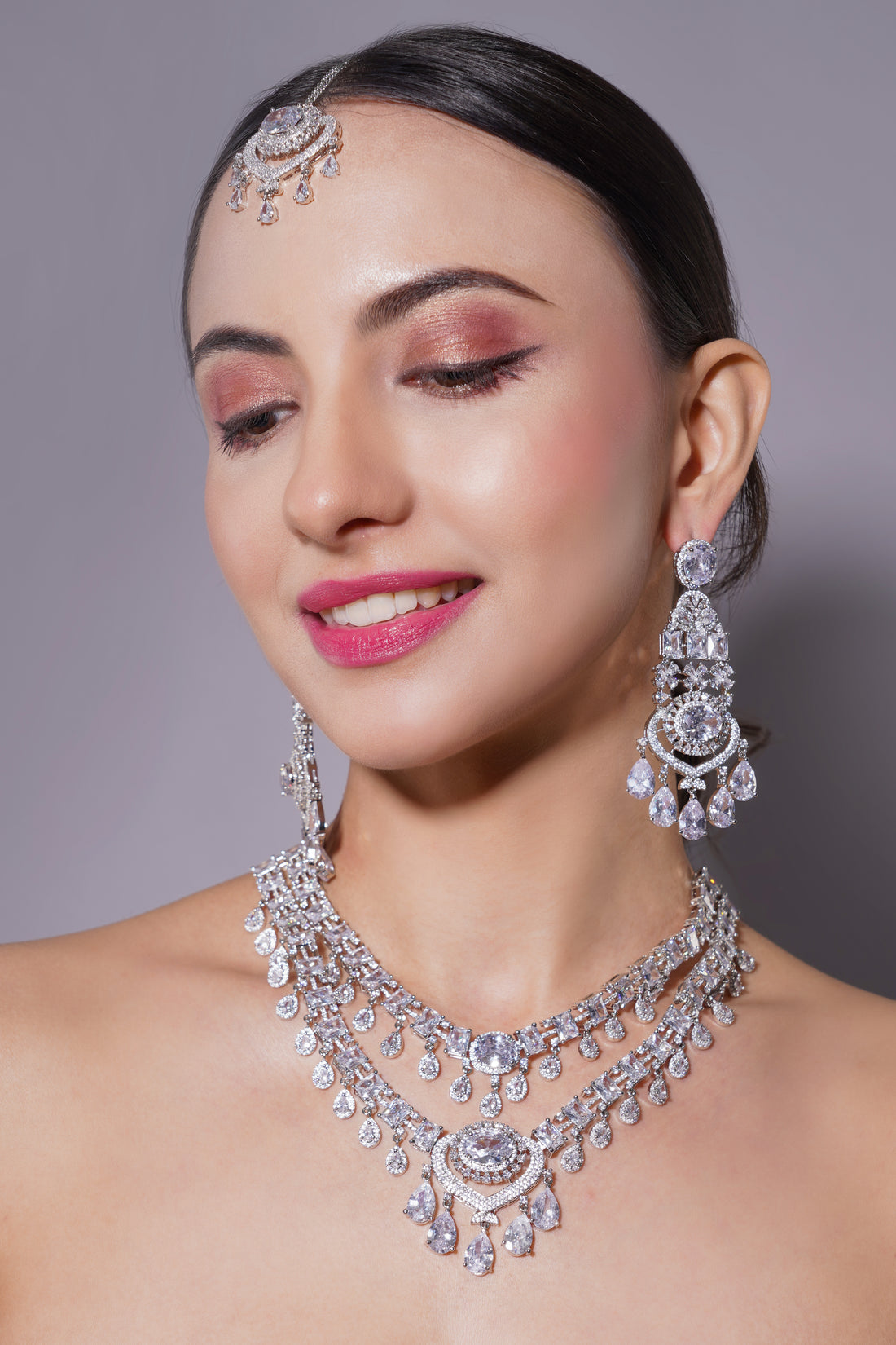 Woman wearing a detailed silver necklace, earrings, and headpiece against a gray background