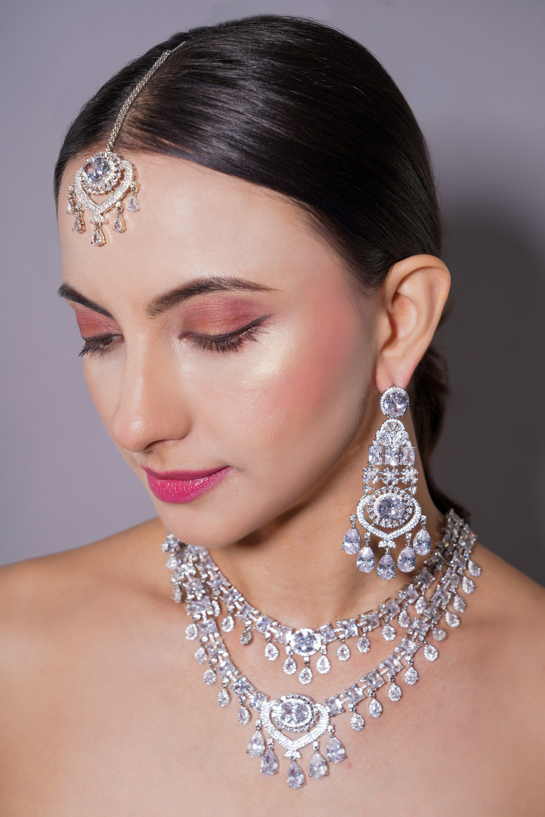 Woman wearing silver jewelry including a headband, earrings, and necklace against a gray background