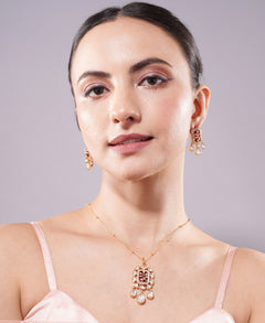 Woman wearing gold jewelry including earrings and a necklace on a plain background