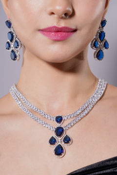Close-up of a woman wearing a diamond and sapphire necklace and earrings on a gray background