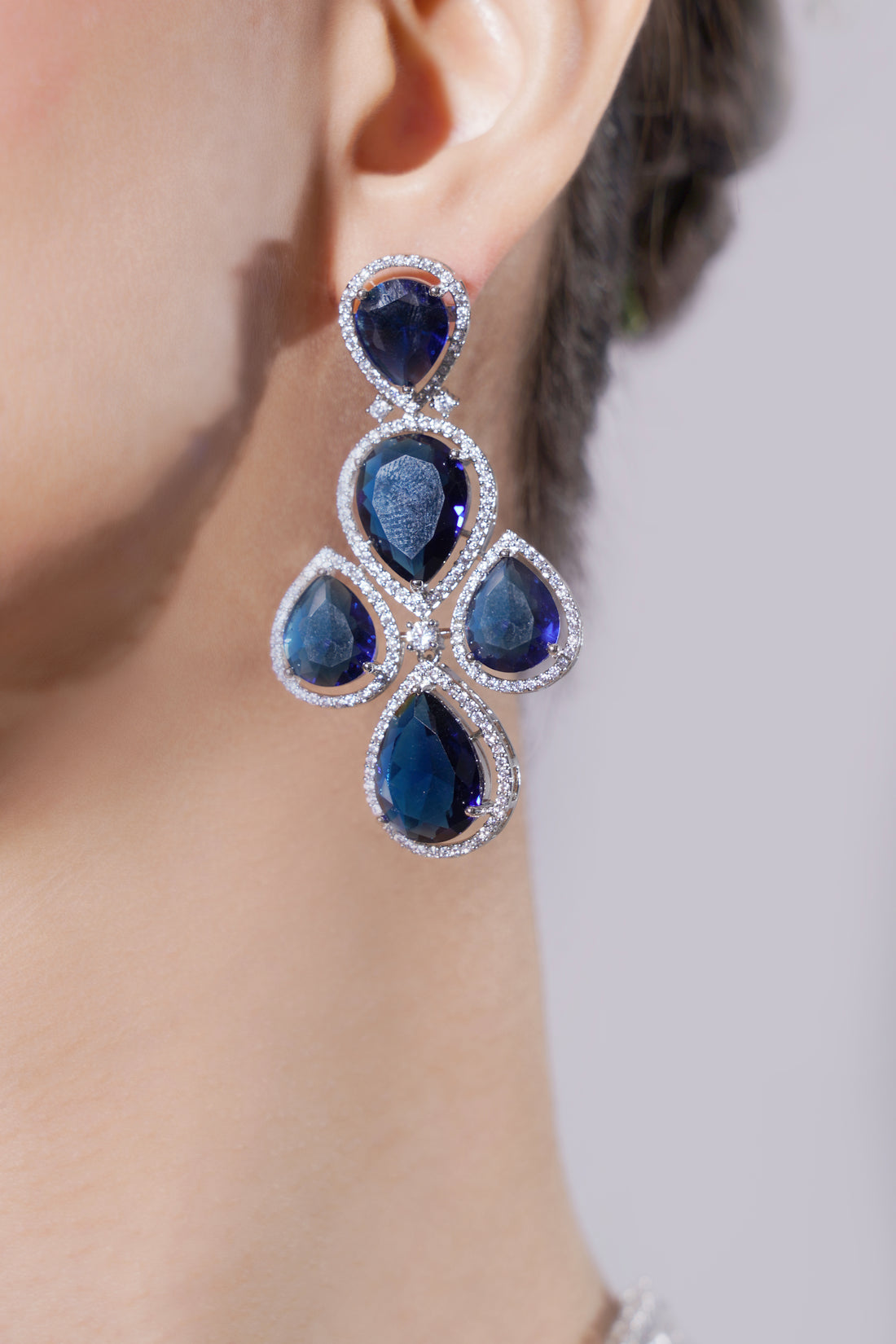 Blue gemstone earrings worn by a person on a neutral background