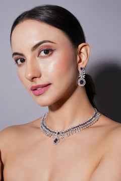 Woman wearing a diamond necklace and earrings against a gray background