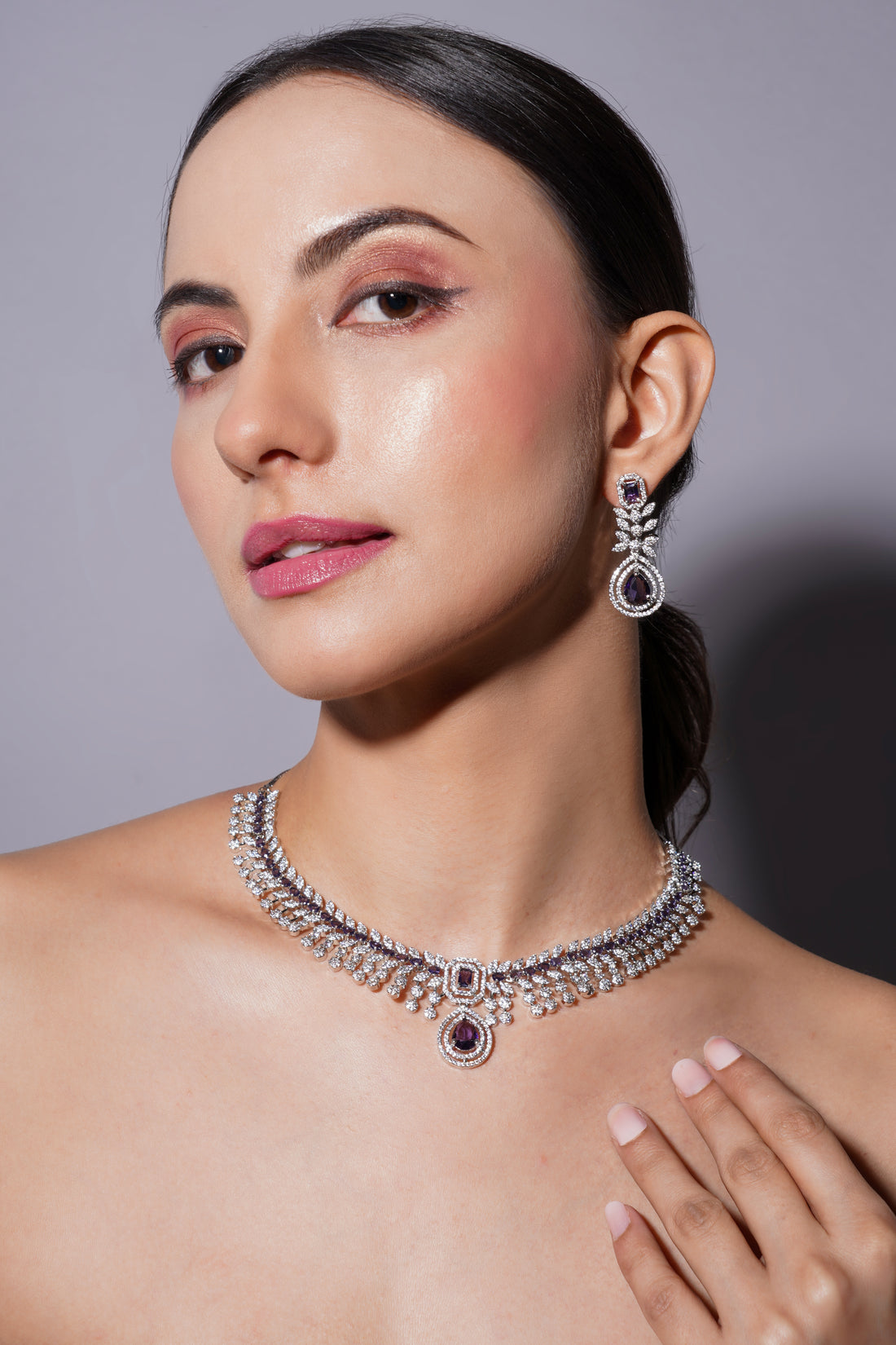 Woman wearing a silver necklace and earrings against a gray background