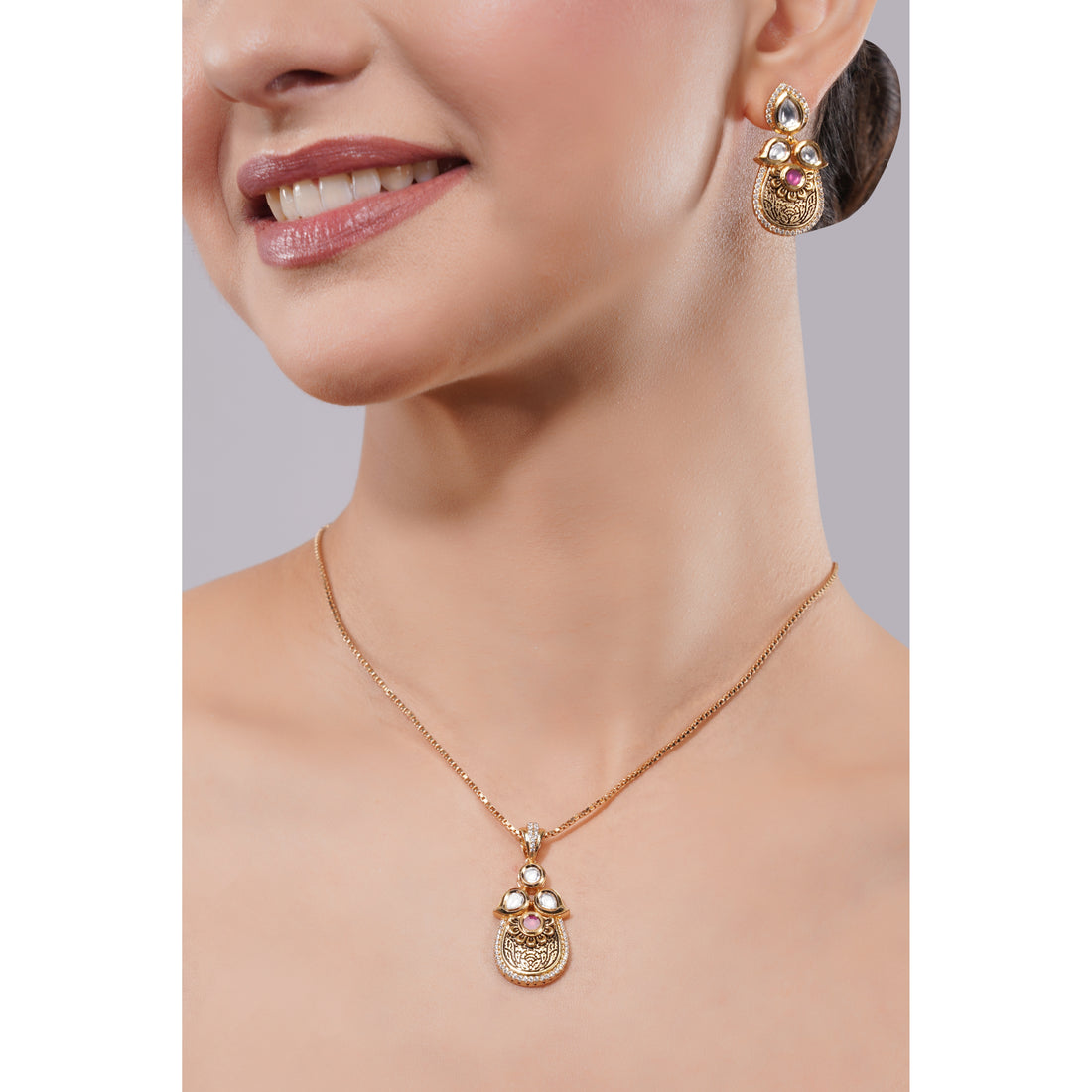 Close-up of a woman wearing a gold necklace and earrings with gemstones on a neutral background.